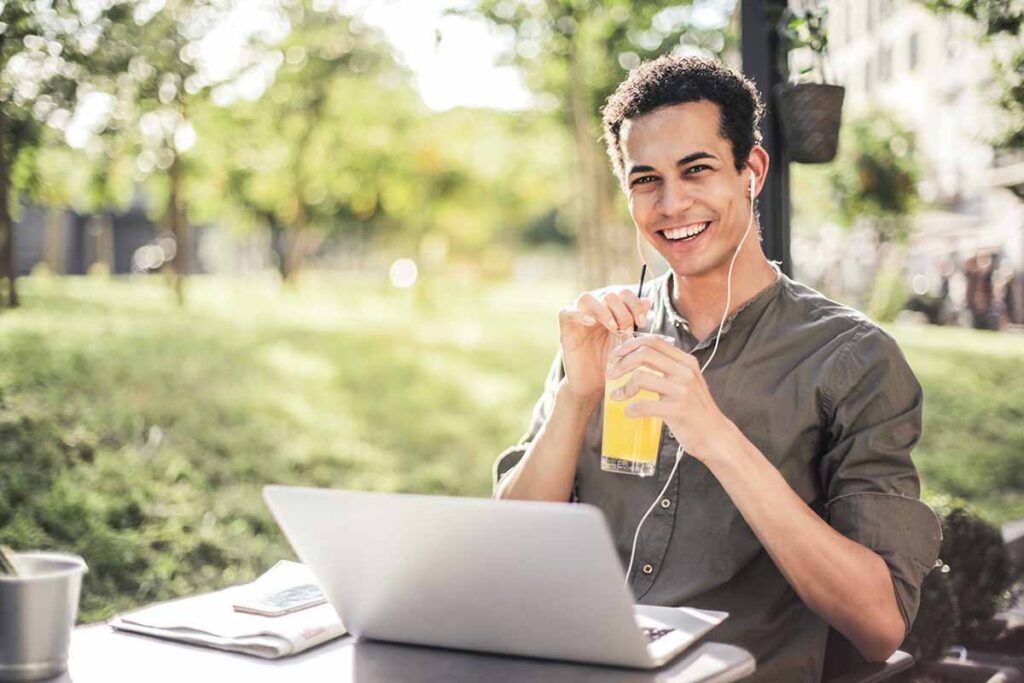 Dieses Foto veranschaulicht einen jungen Mann beim Strompreisvergleich mit Laptop und Limonade in freier Natur.